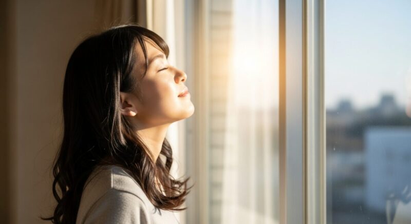 窓辺に立ち、朝日を浴びながら深呼吸する日本人女性