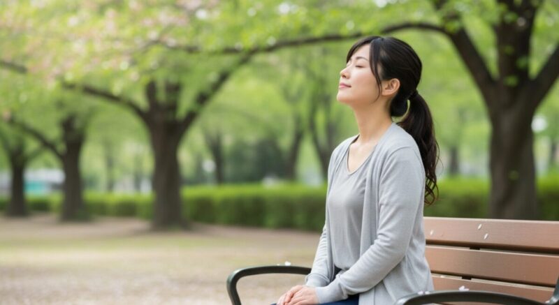 静かな公園のベンチで深呼吸をする日本人女性。少しずつ立ち直ろうとする姿